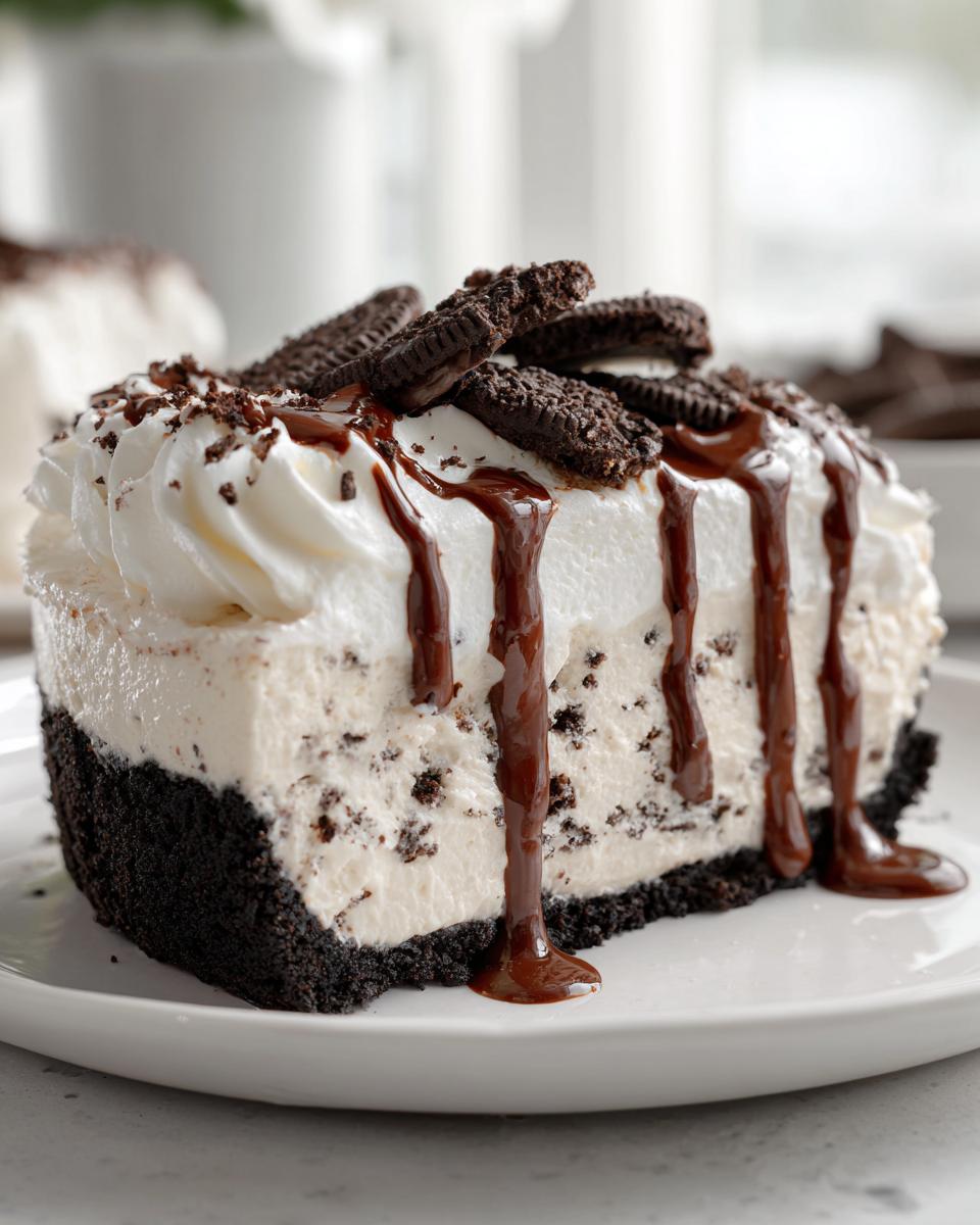 A decadent slice of ice cream pie featuring a dark cookie crust, creamy filling with cookie pieces, whipped topping, and chocolate syrup.