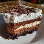 A decadent slice of 4-layer mud pie dessert showing layers of crust, mousse, and whipped topping with chocolate shavings.