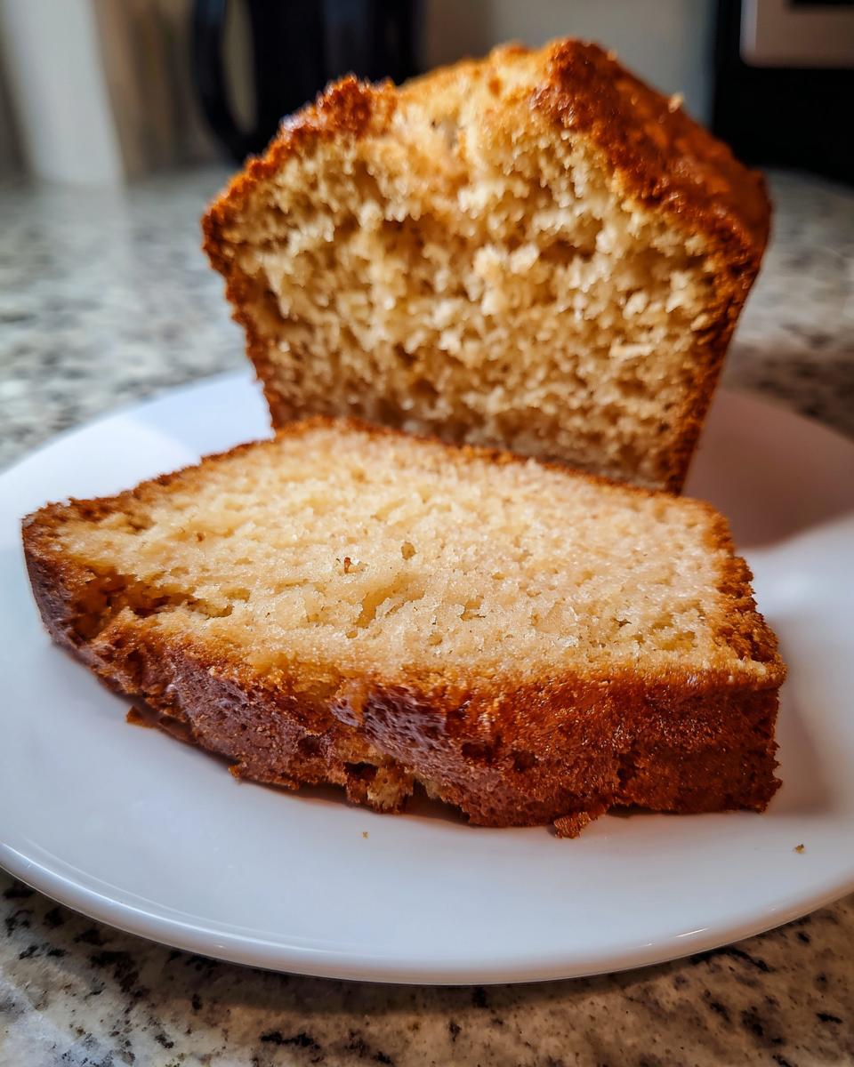 A slice of golden brown beer bread resting in front of the rest of the loaf, showing the soft interior texture.