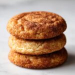 A close-up stack of three soft, chewy snickerdoodles generously coated in cinnamon sugar.