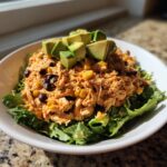 A vibrant bowl of southwest chicken salad mixed with corn and black beans, served over lettuce and topped with diced avocado.