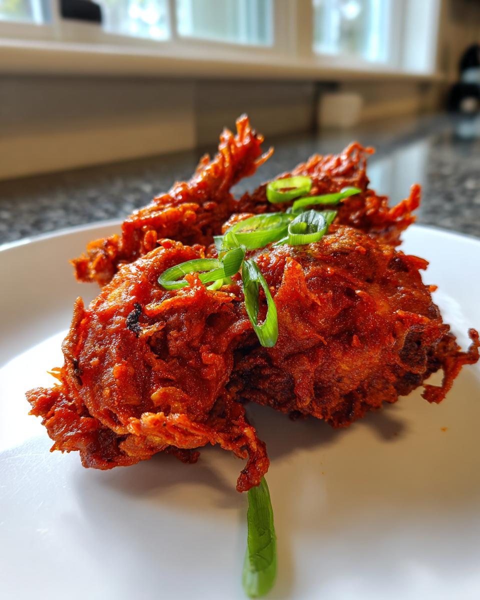 Close-up of crispy, bright red Korean fried chicken pieces garnished with sliced green onions.
