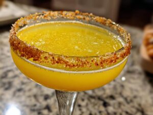 Close-up of a bright yellow lemon drop martini in a coupe glass with a spicy chili-sugar rim.