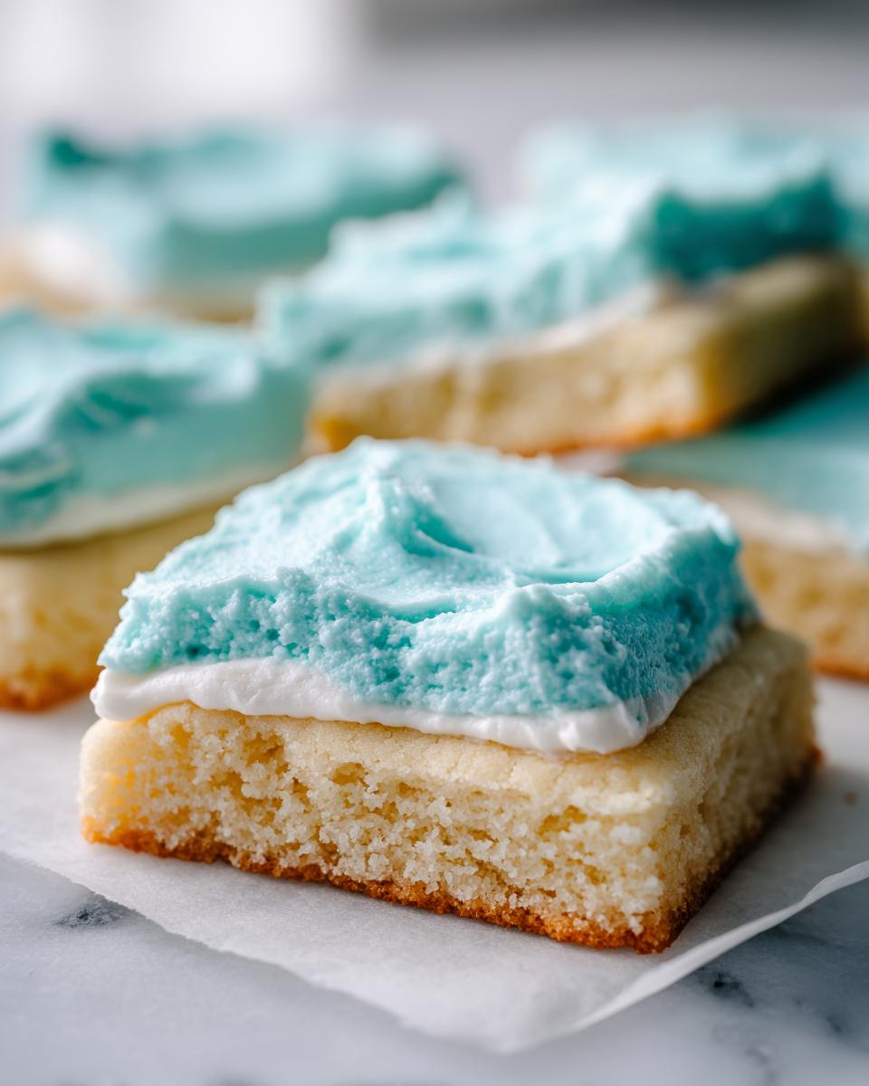 Close-up of a square, thick-cut sugar cookie base topped with white and bright blue frosting.