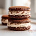 Two stacked chocolate tiramisu cookies filled with creamy mascarpone frosting and dusted with cocoa powder.
