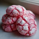 A close-up stack of bright pink, crinkle-topped strawberry cake mix cookies dusted with powdered sugar.