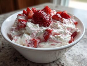 A white bowl filled with creamy, fluffy strawberry cheesecake dip topped with fresh, chopped strawberries.