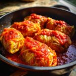 Close-up of tender cabbage rolls topped with rich tomato sauce simmering in a dark pan.