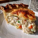 A close-up of a generous slice of turkey pot pie recipe showing flaky golden crust and creamy filling with shredded turkey and vegetables.