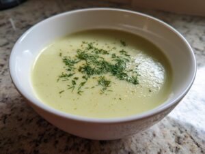Close-up of a bowl of velvety leek soup garnished with fresh dill and spices.