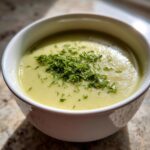 Close-up of a bowl of creamy, velvety leek soup topped with a generous sprinkle of fresh green herbs.