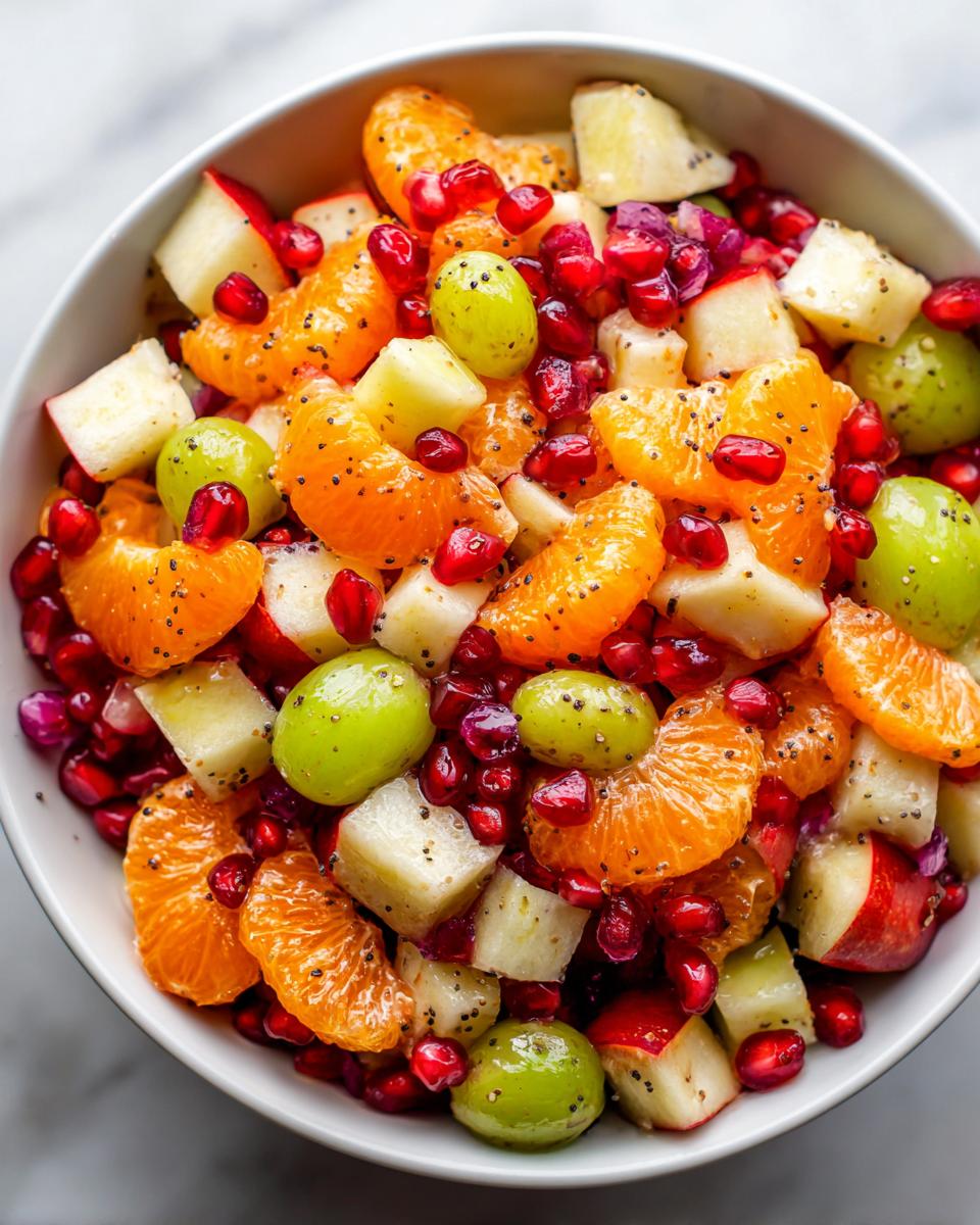 Close-up of a vibrant winter fruit salad featuring mandarin segments, green grapes, pomegranate seeds, and diced apples.