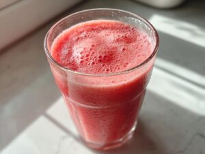 Close-up of a tall glass filled with a vibrant pink watermelon smoothie, showing foam on top.