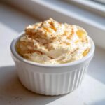 A small white ramekin filled with fluffy, whipped honey butter recipe, dusted with cinnamon.